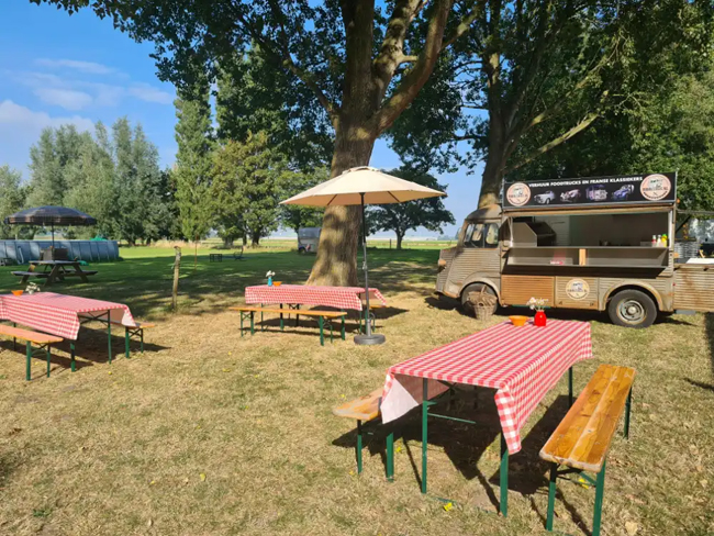 Gezellige zitplaatsen buiten met picknicktafels en een klassieke Citroën HY foodtruck bij 2CV Hoeve Waterrijk